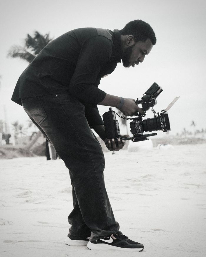 A videographer with camera equipment capturing footage on a sandy beach.